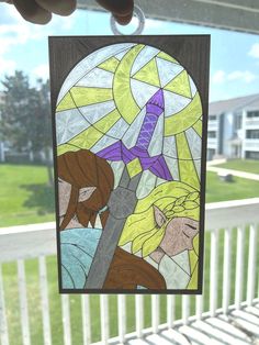 a hand holding up a stained glass window with the image of two women on it