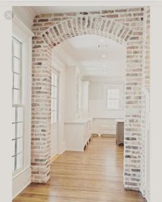 an empty room with wood flooring and brick arches on the wall, leading into another room