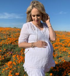 a pregnant woman is standing in a field of flowers with her hand on her hip