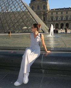 a woman sitting on the edge of a fountain in front of a large glass pyramid