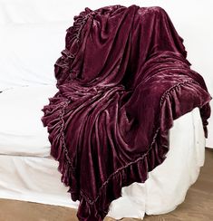 a bed covered in a purple blanket on top of a wooden floor next to a white wall