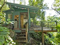 a small green cabin in the woods with stairs leading up to it's entrance