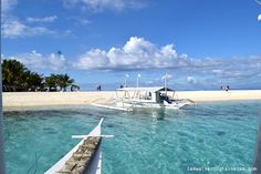 there is a boat that is floating in the clear blue water on the beach and people are walking around it