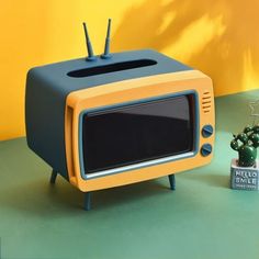 an orange and black television sitting on top of a table next to a potted plant