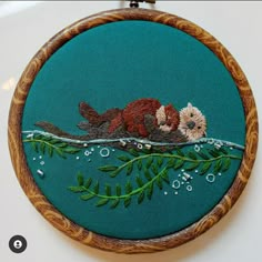 an embroidery kit with two otters sleeping on a branch and bubbles in the water