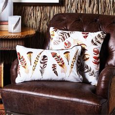 two pillows sitting on top of a brown chair in front of a wall with feathers