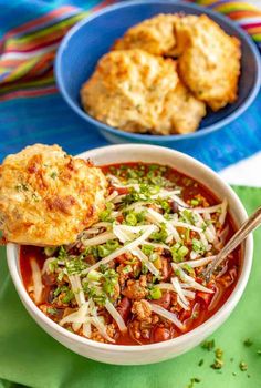 a bowl of soup with meat and vegetables in it next to two plates of biscuits