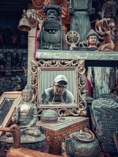 a man is looking at his reflection in a mirror surrounded by decorative objects and other items