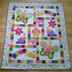 a quilted wall hanging on the floor with many bugs and flowers in different colors