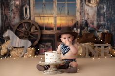 a baby sitting on the floor with a cake in front of him wearing a cowboy hat