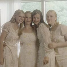 four girls in white dresses standing next to each other with their arms around one another