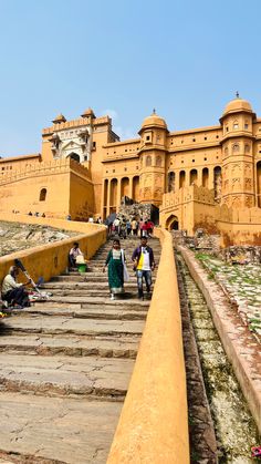 people walking up and down some steps in front of an old building with yellow walls