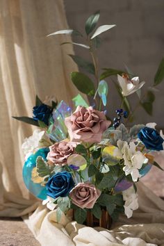 a vase filled with blue and pink flowers on top of a white cloth covered table