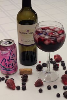 a glass of wine next to a bottle and some berries