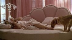 a woman laying on top of a bed next to a dog in a pink room