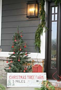 a christmas tree is sitting on the porch next to a sign that says christmas tree farm