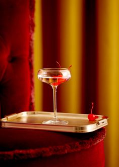 a red velvet chair with a tray holding a drink and a cherries garnish