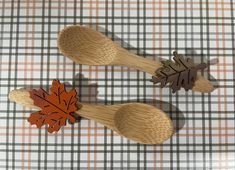 two wooden spoons with leaves on them sitting on a checkered tablecloth surface