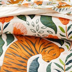 an orange and white tiger print comforter on top of a bed with green leaves