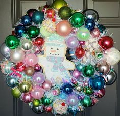 a christmas wreath decorated with ornaments and a teddy bear on the front door, is shown