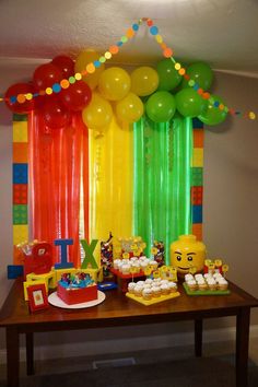 a table topped with cake and balloons next to a rainbow colored wall hanging from the ceiling