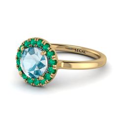 a gold ring with an oval blue topaz surrounded by green stones and the word segit