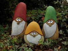 three gnomes made out of rocks sitting on the ground in front of some bushes