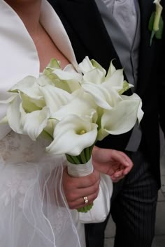 the bride and groom are holding bouquets of white calla lilies in their hands