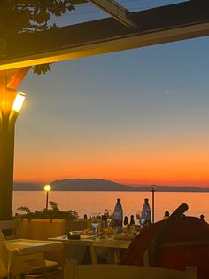 an outdoor dining area overlooking the water at sunset with lights on and people sitting in chairs