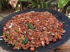 a large pan filled with meat and vegetables on top of a wooden table next to plants