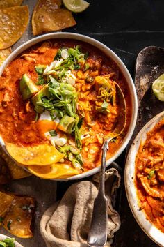 two bowls of chili and tortilla soup with spoons on the side next to them