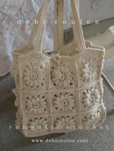 a white crocheted bag sitting on top of a wooden stand next to a bed