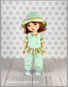 a doll wearing a green outfit and hat with polka dots on the wall behind it