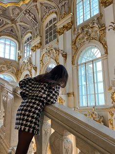 a woman leaning on a railing in front of ornately decorated walls and windows with gold trim