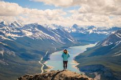 a woman standing on top of a mountain looking down at the valley and lake below