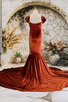 an orange dress on display in front of a wall with flowers and potted plants