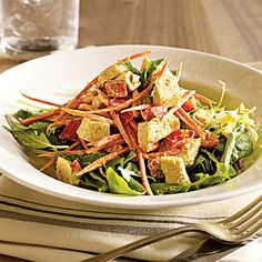 a salad with tofu and carrots in a bowl next to a glass of water