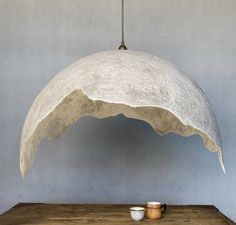 a white lamp hanging from a ceiling over a wooden table with a cup on it