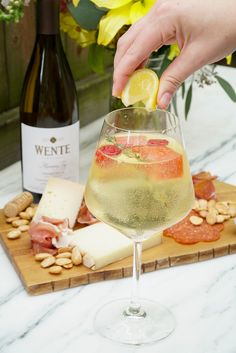 a person holding a lemon wedge over a wine glass filled with white wine and fruit