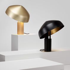 two lamps sitting on top of white pedestals next to each other, one is black and the other is gold