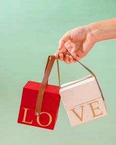 a hand holding a red and white box with the word love hanging from it's handle