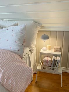 a bed with white sheets and pink gingham comforter next to a night stand