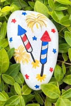 a painted rock sitting in the middle of some leaves with fireworks and stars on it