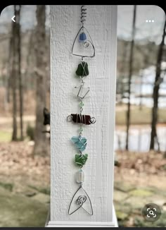 a wind chime hanging on the side of a white pillar with trees in the background