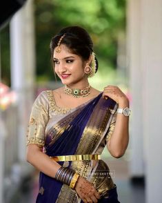 a woman in a blue and gold sari with jewelry on her neck, smiling