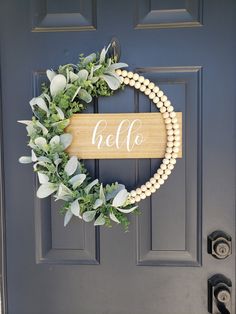 a wreath with the word hello on it hanging on a front door, decorated with pearls and greenery