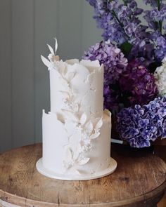 a white wedding cake sitting on top of a wooden table next to purple and white flowers