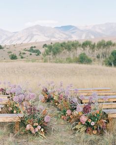 an outdoor ceremony with wooden benches and flowers on the back ground, in front of mountains