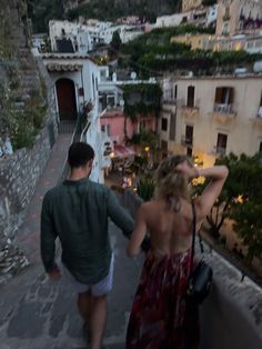 a man and woman walking up the stairs in front of some buildings at night time