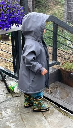 a little boy in rain gear looking at some flowers